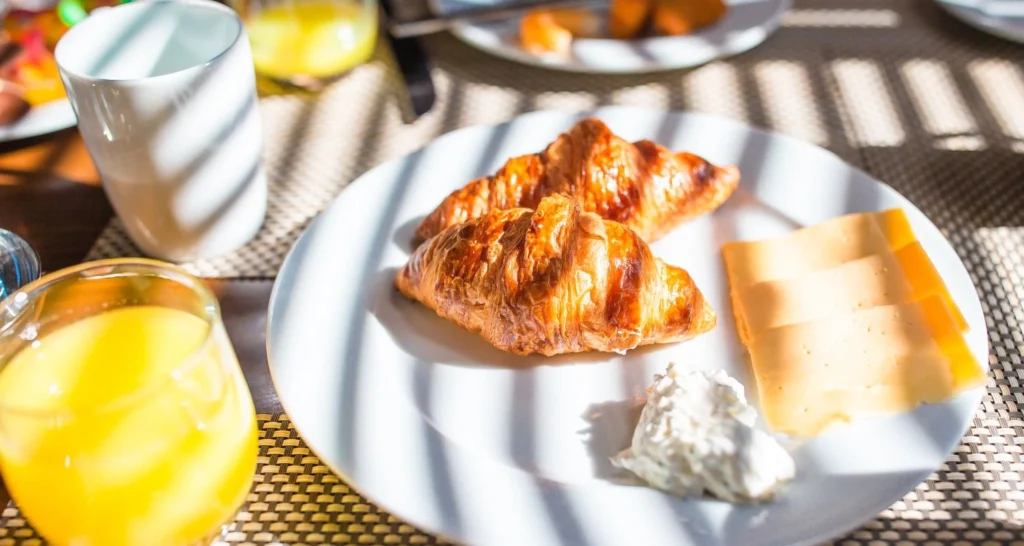 A simple Greek breakfast plate with croissants, sliced cheese, a dollop of cream, and a glass