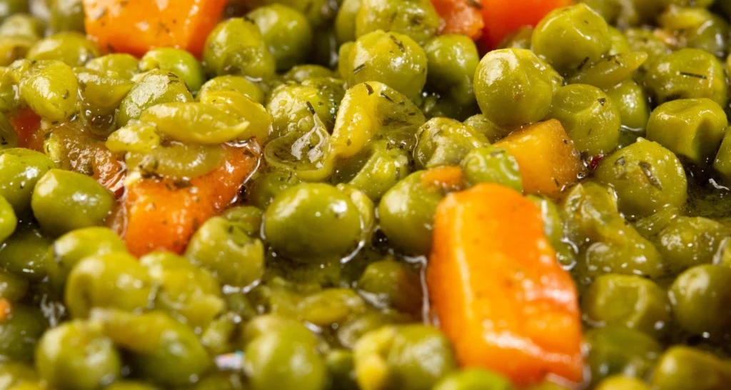 Close-up of cooked peas and carrots in a light herb-infused sauce, showcasing their vibrant colors and texture.