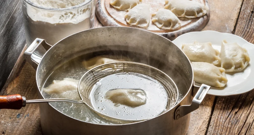 A rustic kitchen scene with vegetarian soup dumplings boiling in a large pot, surrounded by plates of freshly prepared dumplings and a container of flour.