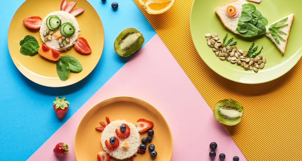 Creative and colorful toddler lunch ideas on plates, featuring animal-shaped sandwiches made with fruits, vegetables, and whole grain bread on a vibrant background.